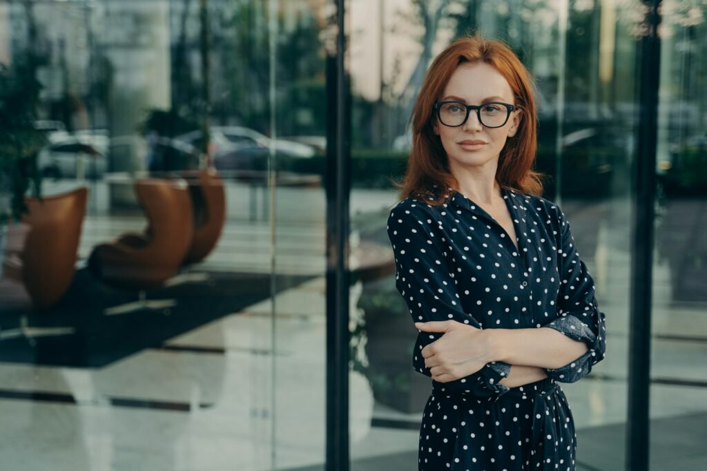 Self assured female director with red hair poses near office building
